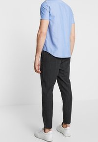 Camicia azzurra a maniche corte, vista posteriore, abbinata a pantaloni neri con righe verticali e sneakers bianche; tessuto liscio e vestibilità moderna.