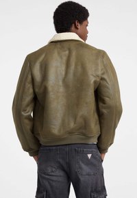 Giacca bomber verde in pelle con colletto in shearling bianco, polsini e orlo a costine. Texture liscia con una finitura leggermente consumata.