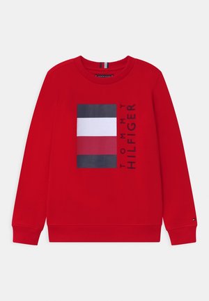 Sweatshirt rouge avec un logo rectangulaire orné de bandes bleu marine, blanches et rouges. Manches et col côtelés, fabriqué en tissu doux.