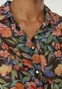 Blommig skjorta med knappar, som har en mörk bakgrund med rosa, orange och gröna mönster. Den har en mjuk textur och en klassisk krage.