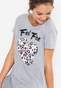 T-shirt grigio a maniche corte con una grafica a cuore di stampa leopardata rosa e testo nero che recita "Sentiti libero di amare." Materiale in cotone morbido.
