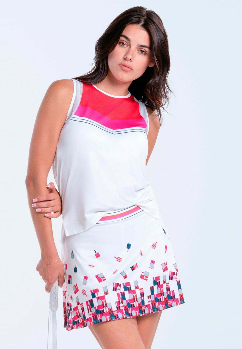 Frau trägt weißes ärmelloses Oberteil mit rotem-pinkfarbenem Brustbereich und weißen Rock mit roten, pinkfarbenen und blauen geometrischen und Paddelmuster.
