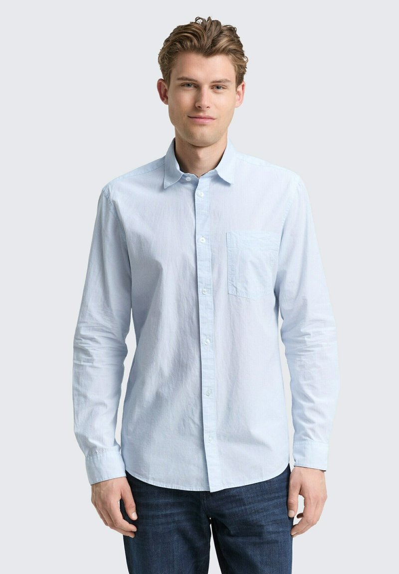 Lichtblauw langemouw blouse met knopen en een borstzak, gemaakt van een textiele katoenstof, gecombineerd met donkerblauwe jeans.
