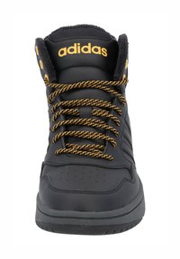 Zapatilla negra de caña alta con acentos amarillos, tela texturizada y cordones con patrón. Presenta perforaciones y un cuello acolchado.