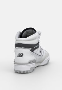 High-top white sneakers with gray accents, made of synthetic materials, featuring a padded collar, textured surface, and rubber sole.