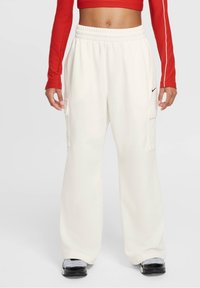 Bílé cargo kalhoty s volným střihem, elastickým pasem, bočními kapsami a malým černým logem Nike na přední straně. Hladká textilie.
