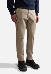 Beige cargobroek met zijzakken, tan stof, licht taps toelopende pijp, gecombineerd met zwarte schoenen en een marineblauwe sweatshirt.