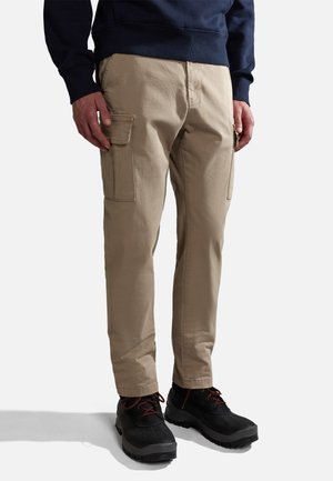 Beige cargo bukser med sidelommer, lysebrunt stof, let tapered ben, parret med sorte sko og en marineblå sweatshirt.