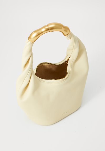 Κρεμ δερμάτινη τσάντα χεριού με στριφτό σχέδιο και χρυσό, καμπύλο χερούλι. Διαθέτει κλείσιμο με φερμουάρ και ομαλή υφή. Το εσωτερικό είναι καφέ.