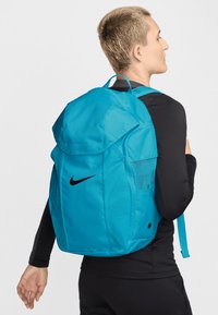 Turkis Nike ryggsekk med avrundet topp, polstrede remmer, mesh sidelomme og fremtredende svart swoosh-logo på siden.