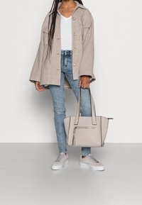 Beige oversize bunda se směsí vlny, bílá košile s výstřihem do V, světle modré úzké džíny, šedá kožená taška na zip a šedé tenisky s bílou podrážkou.