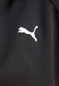 Black textured fabric features a white leaping Puma logo, displaying a smooth design. The logo contrasts sharply with the dark background.