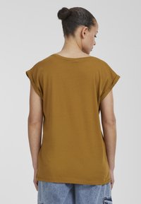 Brun oversized t-shirt med uppvikta ärmar, tillverkad av bomull, med rund halsringning och avslappnad passform, i kombination med blå denimshorts.
