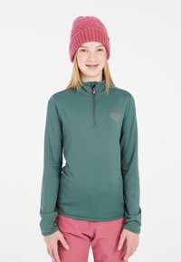 Groene langemouwpullover met een kwart rits en een roze rits. Voorzien van een ski-logo, gedragen met roze broek en een getextureerde roze gebreide beanie.
