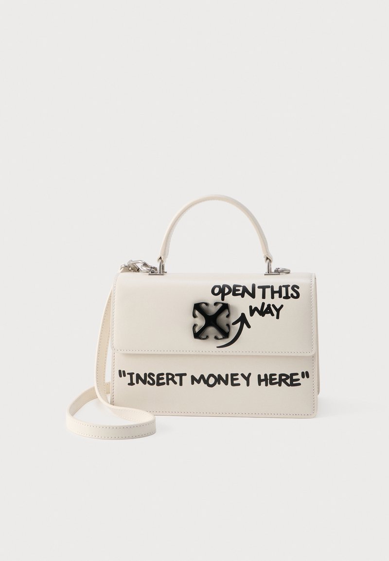 Τσάντα χειρός κρεμ χρώματος με μαύρο κείμενο "ΑΝΟΙΞΤΕ ΑΠΟ ΕΔΩ" και ένα βέλος κοντά στο κούμπωμα, και "ΒΑΛΤΕ ΛΕΦΤΑ ΕΔΩ" στο μπροστινό καπάκι.