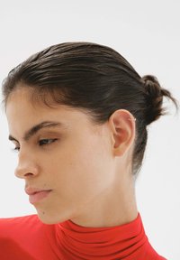 Pendiente de oro en una modelo con el cabello recogido hacia atrás, vistiendo un suéter de cuello alto rojo. Enfoque en el detalle de la oreja y la textura suave de la piel.