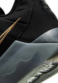 Κοντινή λήψη μαύρου και γκρι αθλητικού παπουτσιού με χρυσό λογότυπο Nike και λεπτομέρειες υφής στη λαστιχένια σόλα.