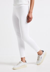 Leggings blancs à la coupe ajustée, texture lisse et taille élastique. Associés à des baskets blanches avec des accents marins contrastants.
