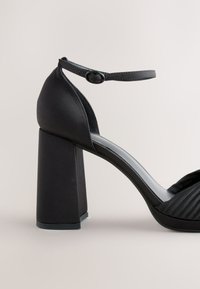 Fekete magas sarkú szandál selyemfényű felülettel, blokk sarokkal, bokapánttal és texturált redőzéssel az elején, sima talppal.