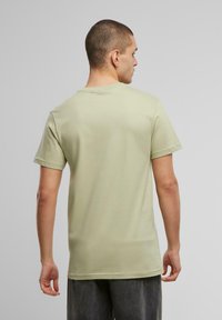 Camiseta de algodón verde claro con mangas cortas y escote redondo, mostrada desde la parte de atrás, que muestra una textura suave y un diseño minimalista.