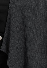 Svart stickad sjal med ribbad textur. Har en lös, flödande design och ett mjukt tyg som ger en subtil lyster.