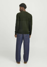 Pull en maille vert avec des rayures horizontales texturées, poignets et ourlet côtelés ; associé à un jean en denim bleu ample et des chaussures marron.