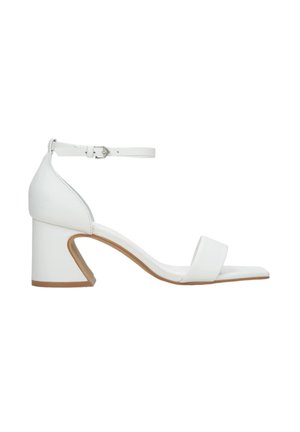 White leather heeled sandals with an ankle strap, square toe, and a unique triangular block heel design. Smooth texture and minimalist style.