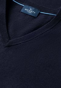 Maglione a V color blu navy scuro con colletto a costine e etichetta Hackett London all'interno del collo, con un bordo interno azzurro chiaro.