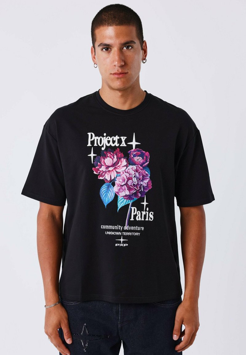 Camiseta de algodón negra con un atrevido diseño gráfico floral en rosa y púrpura, con texto en blanco y embellishments adicionales en la tela.