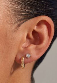 Boucle d'oreille en or avec un design torsadé et un petit clou mettant en vedette un gemme rond clair. Gros plan sur l'oreille et les boucles d'oreilles.