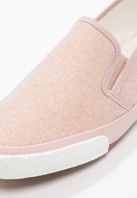 Gros plan d'une chaussure à enfiler rose clair avec tige en tissu texturé et semelle en caoutchouc blanche à motifs.