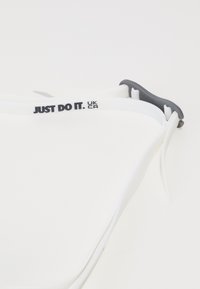 Hvid sportsarmbånd med prægede sorte bogstaver "JUST DO IT." og grå accenter; fleksibelt materiale med en glat tekstur.