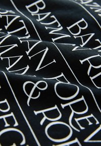 Čierna tkanina s hladkým povrchom s bielym textom v rôznych písmach. Text obsahuje "BATMAN," "FOREVER," a "& ROBIN."