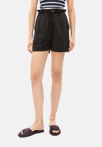 Black shorts with a relaxed fit, elastic waistband, and drawstring. Paired with black slide sandals. Smooth texture, knee-length cut.