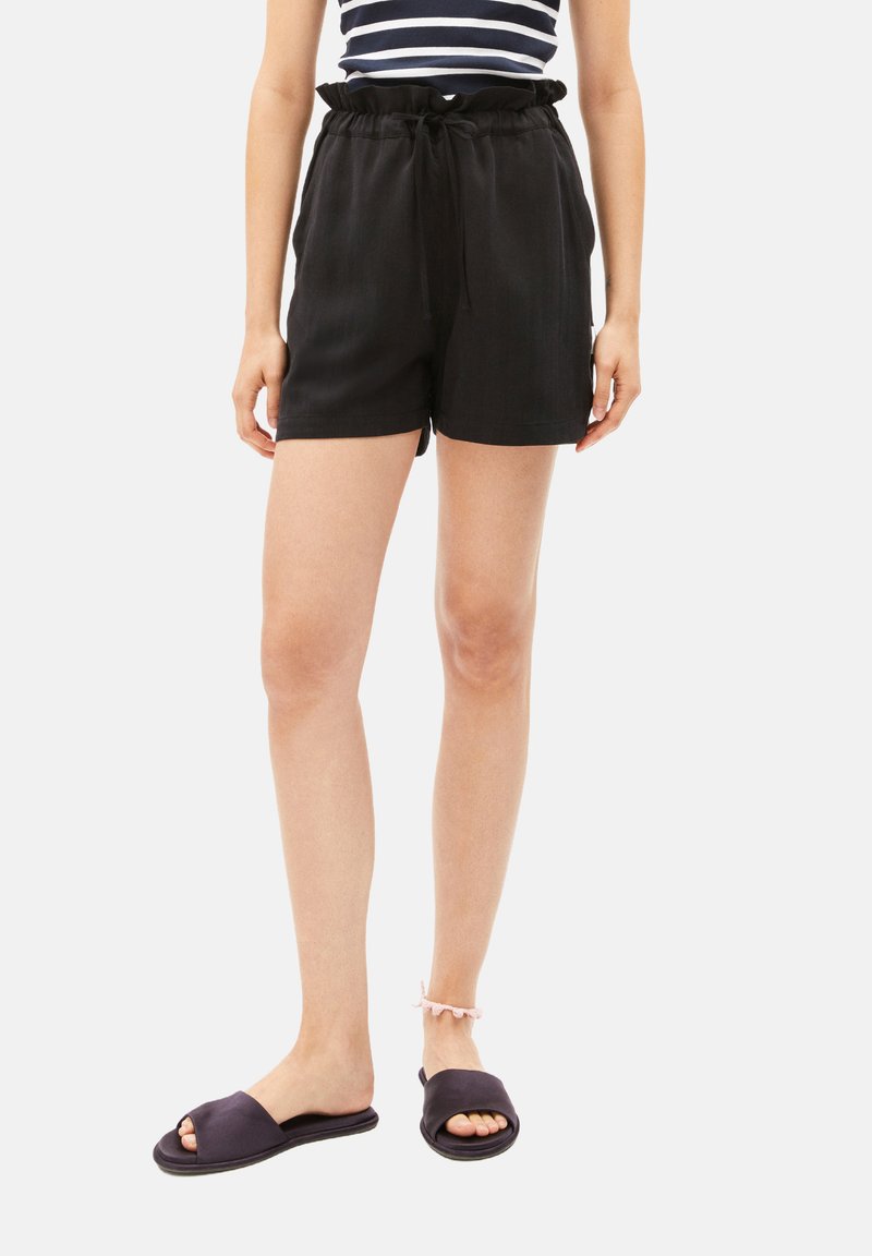 Black shorts with a relaxed fit, elastic waistband, and drawstring. Paired with black slide sandals. Smooth texture, knee-length cut.