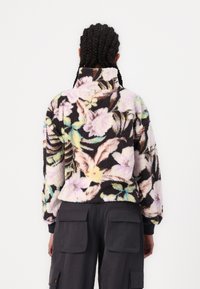 Miękki pulower z wysokim kołnierzem w wielokolorowy wzór kwiatowy na czarnym tle. Posiada ściągacze na mankietach i luźny fason.