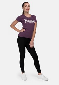 Purple cotton T-shirt with white "Lonsdale London" print, paired with black leggings and white sneakers. Simple, fitted design.