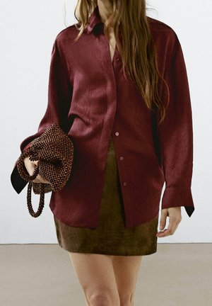 Maroon, textured button-up shirt with a relaxed fit, paired with a brown suede skirt. The shirt features a collar and long sleeves.
