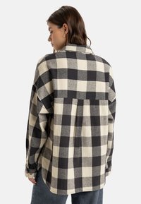 Black and cream checkered button-up shirt, with a relaxed fit, pleated back detail, and long sleeves, made from a soft, textured fabric.
