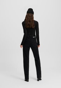 Pantalones de pana negros de talle alto con un diseño de pierna recta y dos bolsillos traseros. Combinados con una camiseta negra ajustada de manga larga y un gorro de canalé.