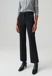 Pantaloni neri su misura con pieghe frontali, design a gamba dritta, vita medio-alta, abbinati a un maglione in maglia grigia e stivali neri con tacco.