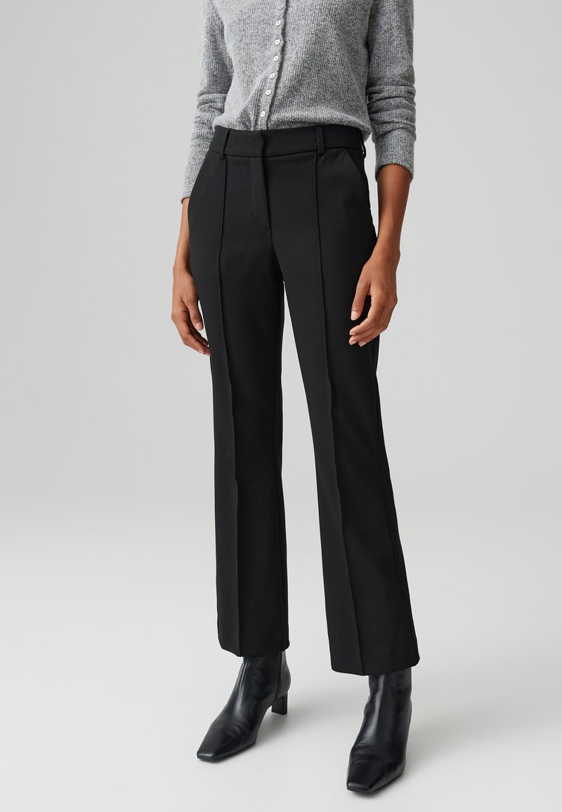 Pantaloni neri su misura con pieghe frontali, design a gamba dritta, vita medio-alta, abbinati a un maglione in maglia grigia e stivali neri con tacco.