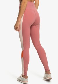 Pink leggings with a color-block design featuring blush and orange accents. Made of stretchy material with a high waistband.