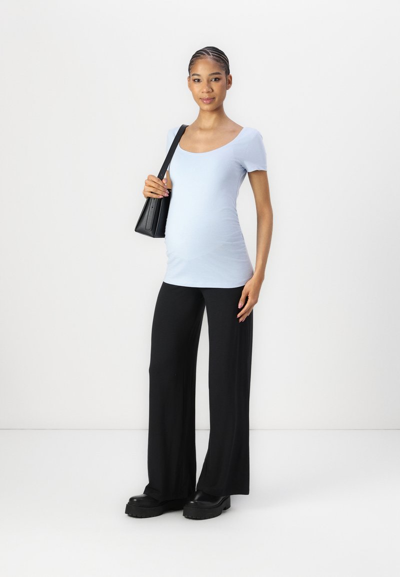 Light blue, fitted, short-sleeve top paired with loose black trousers. Model holds a small black handbag and wears chunky black shoes.