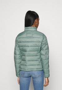 Giacca a vento verde chiaro con colletto alto, design trapuntato e polsini elasticizzati. Realizzata in materiale lucido, con una leggera lucentezza.