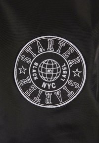 Patch circulaire brodé en noir et blanc avec "STARTER", un globe, des étoiles et le texte "NYC BLACK LABEL" sur tissu noir.