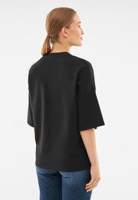 Tricou negru supradimensionat cu mâneci scurte, fabricat din bumbac. Designul are un gât rotund și o croială confortabilă.