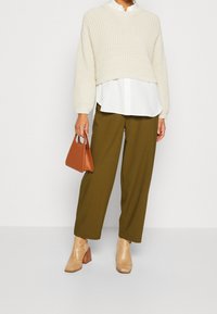 Un pull court en tricot crème porté sur une chemise blanche, un pantalon large olive, un sac à main en cuir marron et des bottines texturées beige.