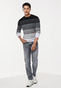 Suéter de rayas de manga larga en tonos gris, negro y gris claro. Combinado con jeans grises desgastados y zapatillas blancas.