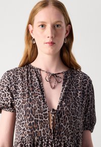 Kjole med leopardmønster som har dyp V-hals, justerbar snøring, korte puff ermer og utsvingt bunn. Mykt, lett stoff.
